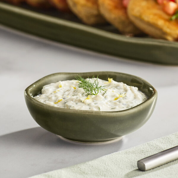 A round Acopa Juniper Green China sauce cup filled with white sauce and lemon wedges.