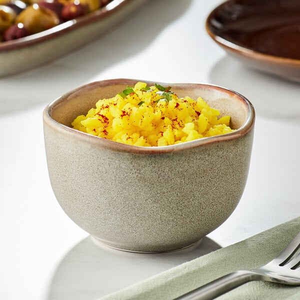 A close-up of a brown bowl filled with yellow rice with spices.