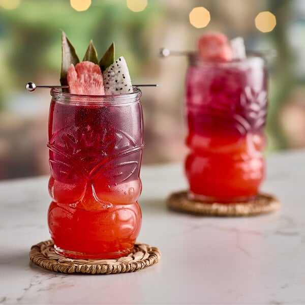 Two glasses of red and pink Tiki Breeze energy drinks with fruit on a table.