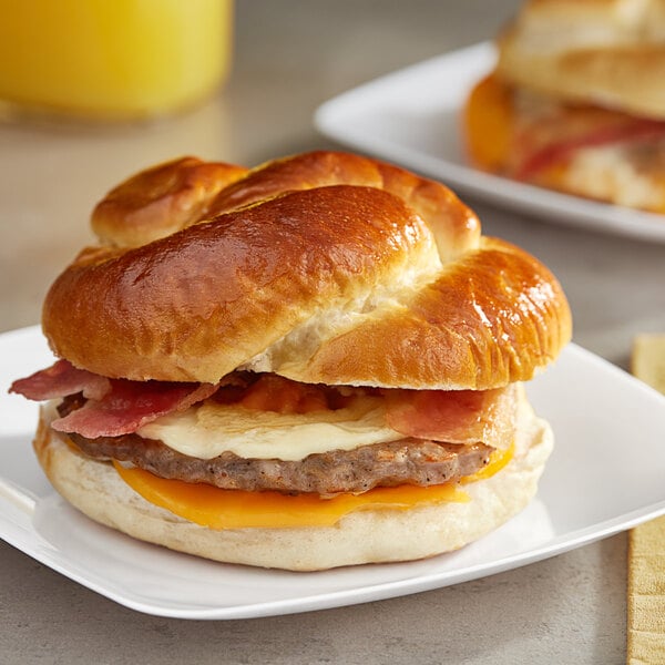 A Grand Prairie sausage, bacon, and cheese pretzel bun breakfast sandwich on a white plate.