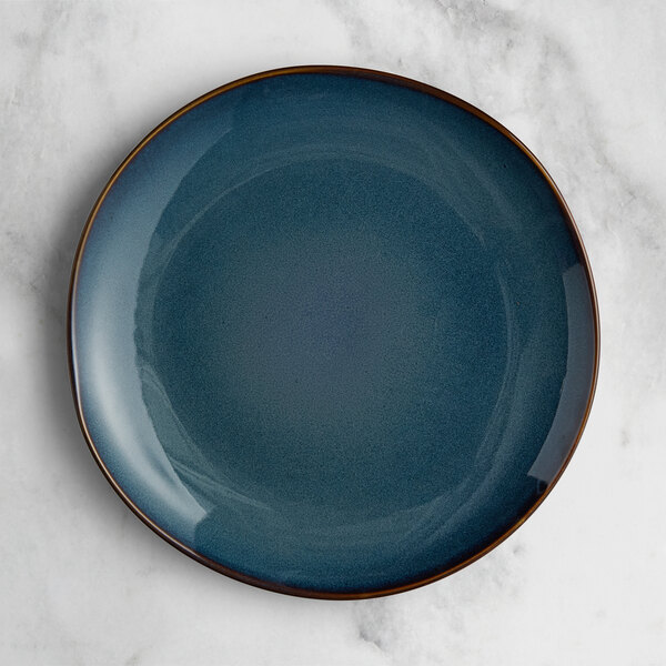 An Acopa Highlands skyfall blue coupe china plate with a brown rim on a marble surface.