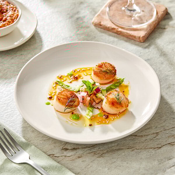 An Acopa Highlands white coupe plate on a table with food and a glass of wine.