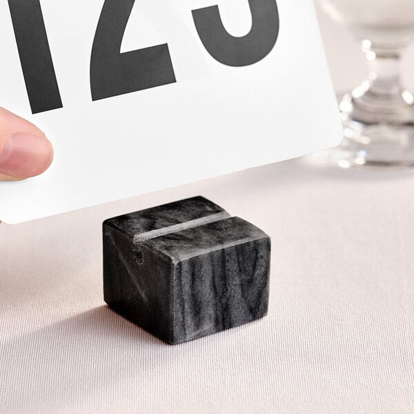 A hand holding a card over an American Metalcraft black marble cube with a card in it.