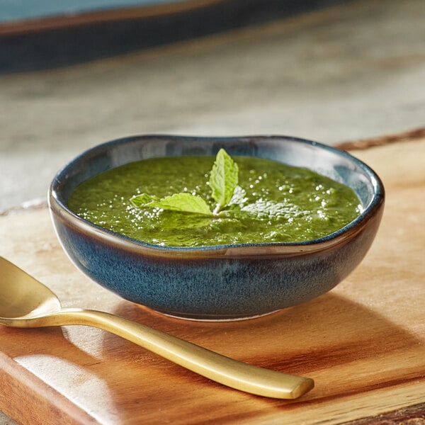 A bowl of green sauce in an Acopa Highlands skyfall blue sauce cup with a spoon.