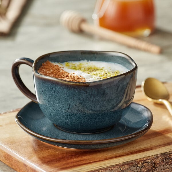 A Skyfall blue china cup of coffee with white foam and brown powder on a wood surface.