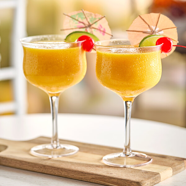 Two glasses of mango smoothie with umbrellas and cherries on top.