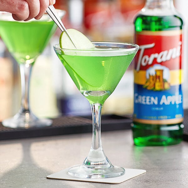 A person pouring Torani Green Apple flavoring into a glass with a green drink.