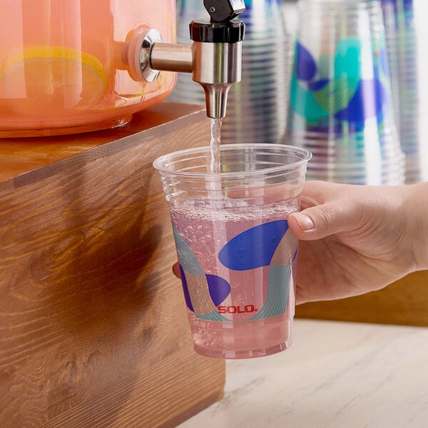 A hand holding a Solo plastic cup with a drink being poured into it.