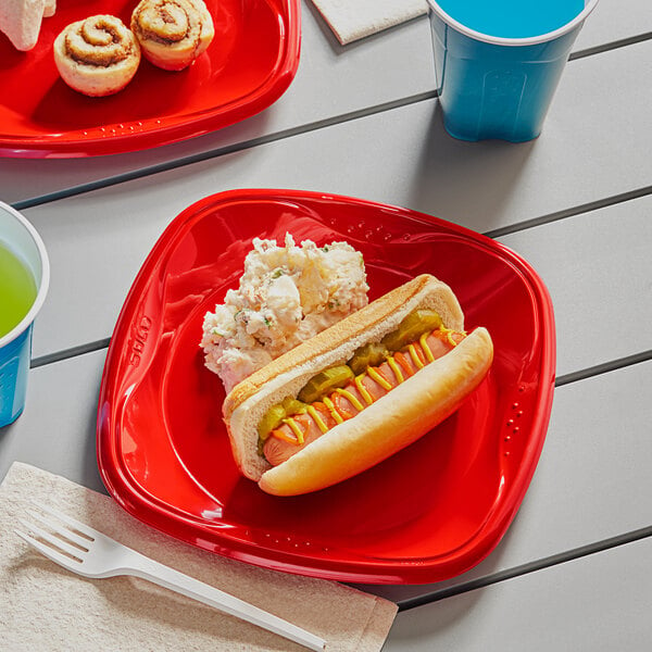 A Solo Squared red plastic plate with a hot dog, mashed potatoes, and a blue cup with a white top on a table.