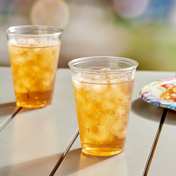 Two Solo clear plastic cups filled with ice tea on a table.