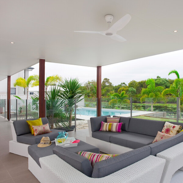 A patio with a white couch and a yellow pillow in the middle of a modern outdoor living area.