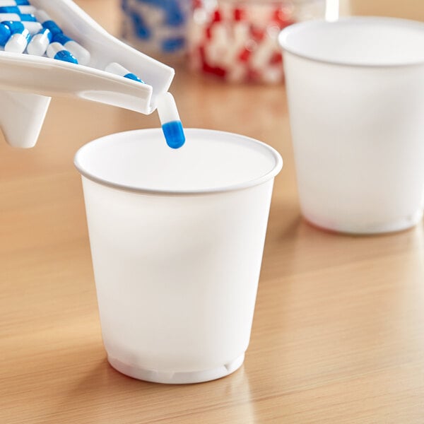 A person pouring a blue capsule into a Solo white plastic refill cup.