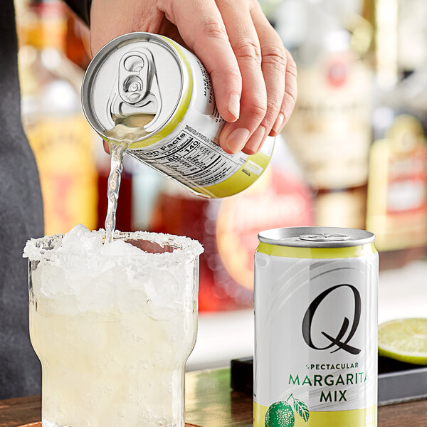 A person pouring Q Mixers Premium Margarita mix from a can into a glass with ice.