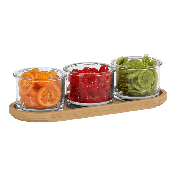 A Cal-Mil faux wood condiment organizer with 3 round glass jars filled with orange slices, cherries, and dried kiwi slices.