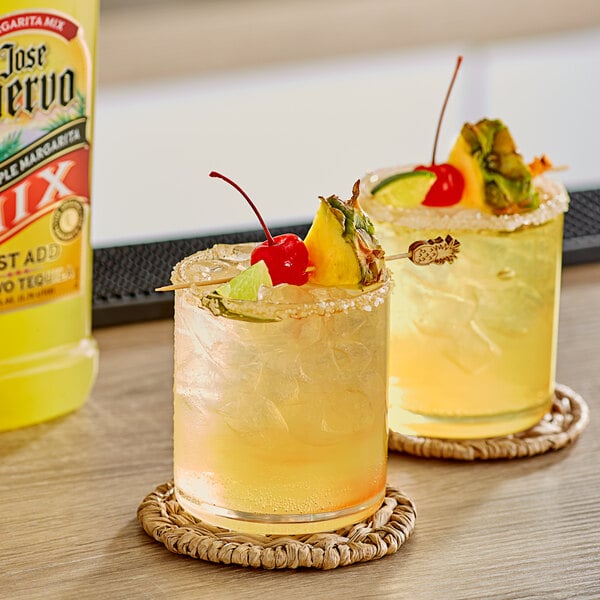 Two glasses of Jose Cuervo Pineapple Margarita with fruit on top on a table.