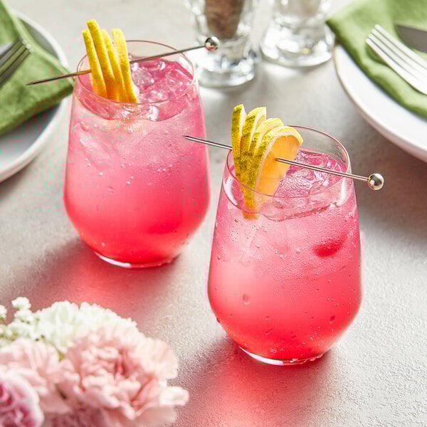 Two glasses of pink prickly pear drinks with straws and lemon slices.