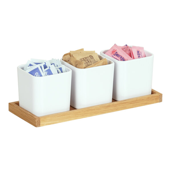 A Cal-Mil oak condiment organizer with three white square containers on a counter.