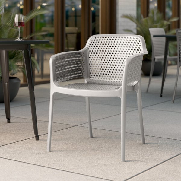 A white Lancaster Table & Seating Rio Cool Oyster Gray resin arm chair on an outdoor patio.