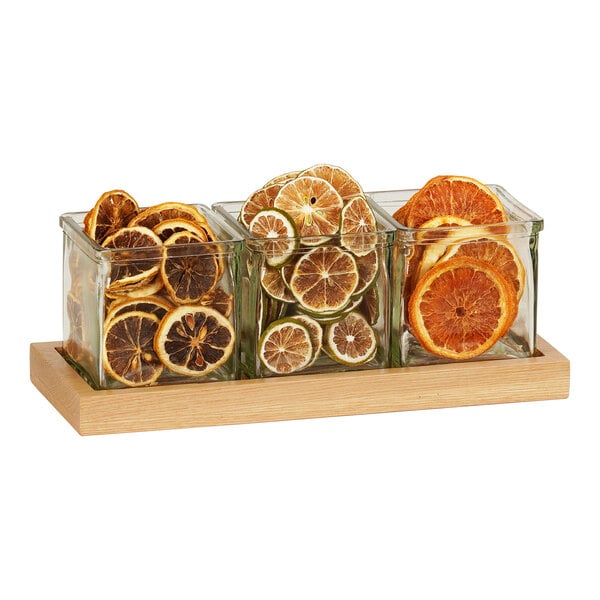 A Cal-Mil oak condiment organizer with three square glass jars full of citrus slices.