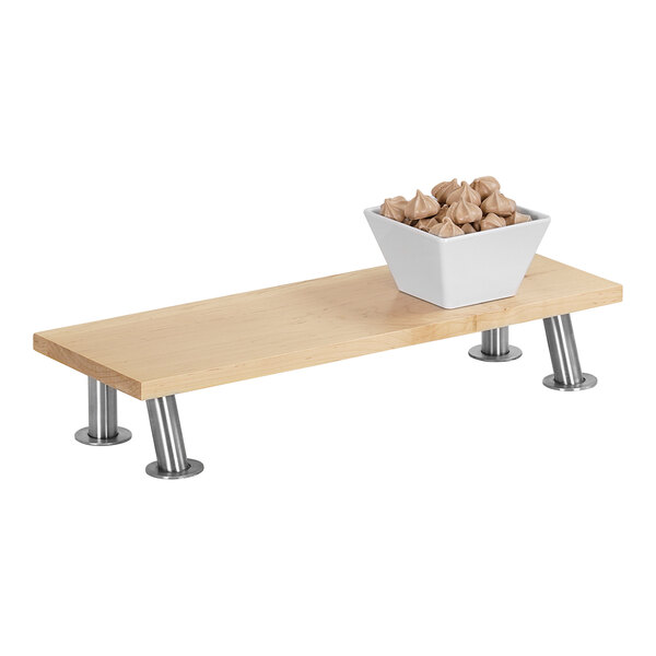 A Cal-Mil maple rectangle display stand with stainless steel legs holding a bowl of brown food on a wooden table.
