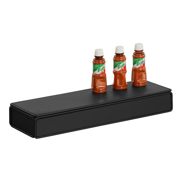 A group of bottles of hot sauce on a black rectangular Cal-Mil display stand.