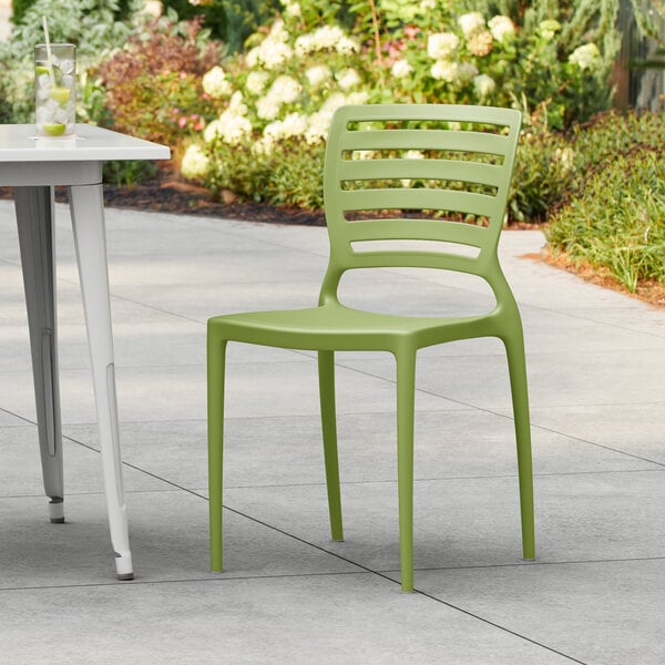 A Lancaster Table & Seating Sol Sea Moss Green resin chair on a table on an outdoor patio.