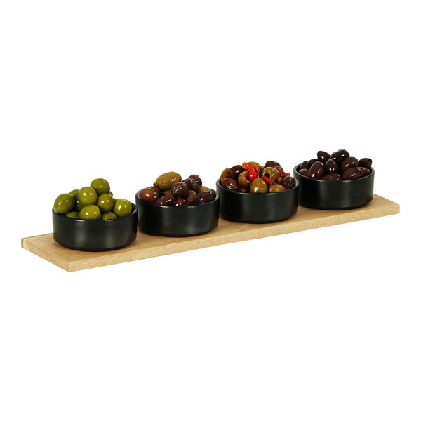 A Cal-Mil oak rectangular serving board with a row of black bowls of olives on it.