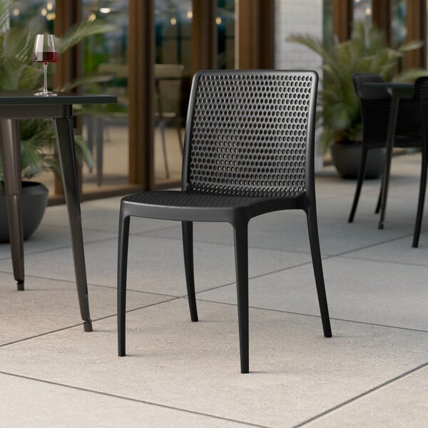 A black Lancaster Table & Seating Rio stone resin side chair on an outdoor patio.