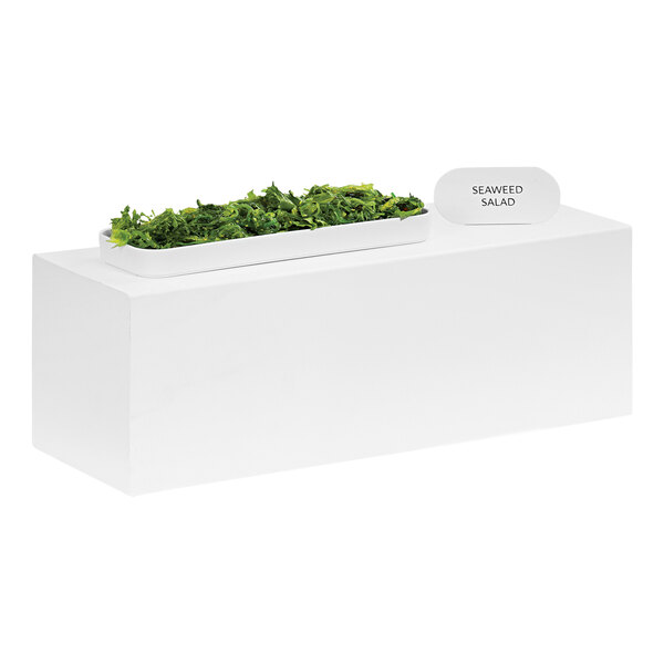 A white rectangular metal display stand holding a bowl of green leaves.