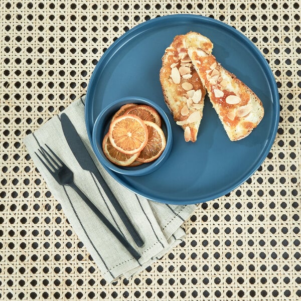 A Cal-Mil stone blue melamine plate with food, a slice of orange, and a bowl of orange slices with a fork and knife.