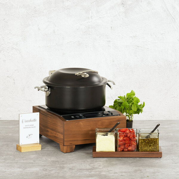 A walnut countertop induction range with a black pot, accompanied by jars of ingredients and a small plant.