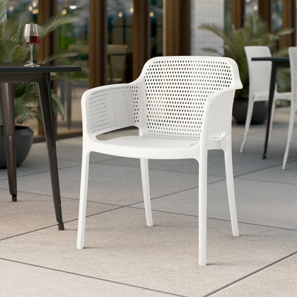 A white Lancaster Table & Seating Rio resin arm chair at a table on a patio.