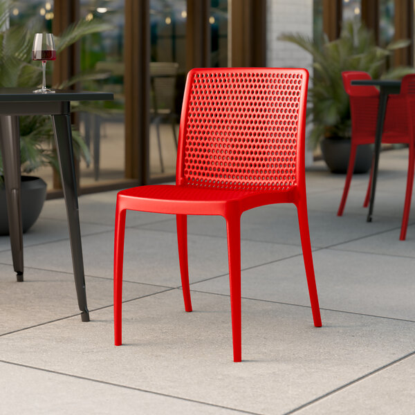 A red Lancaster Table & Seating Rio Buoy resin side chair on an outdoor patio next to a table with a glass of wine.