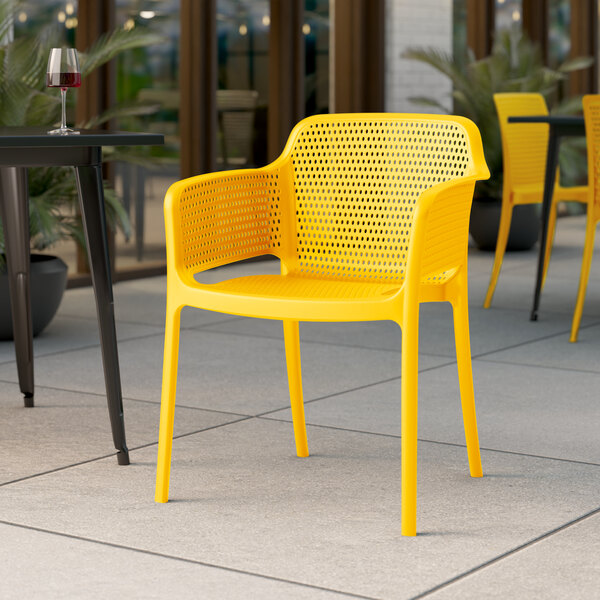 A Lancaster Table & Seating Rio Sunshine Yellow resin arm chair sits at a table on an outdoor patio.