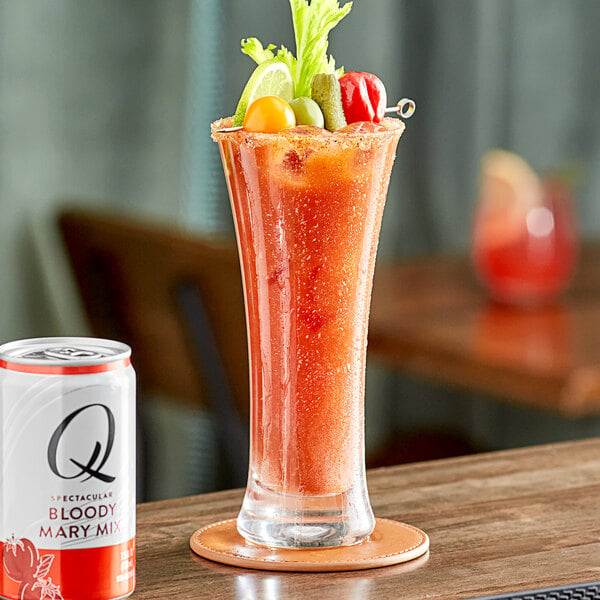 A glass of a red drink with a white can of Q Mixers Premium Bloody Mary Mix on a table.