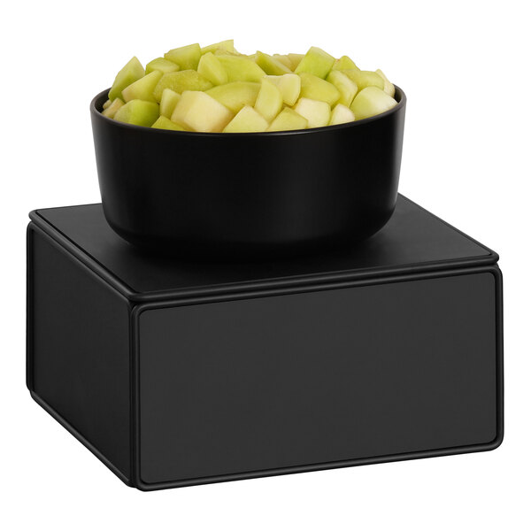 A black metal cube display stand with a bowl of cut green apples on top.