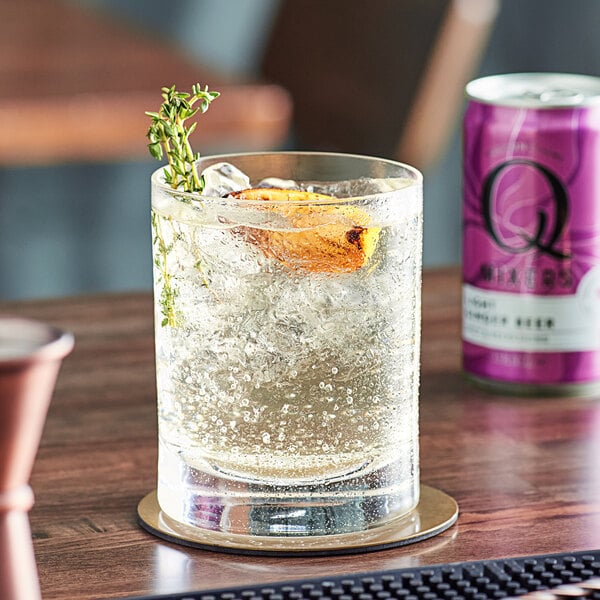 A glass of clear liquid with bubbles and a purple and white Q Mixers Light Ginger Beer can.