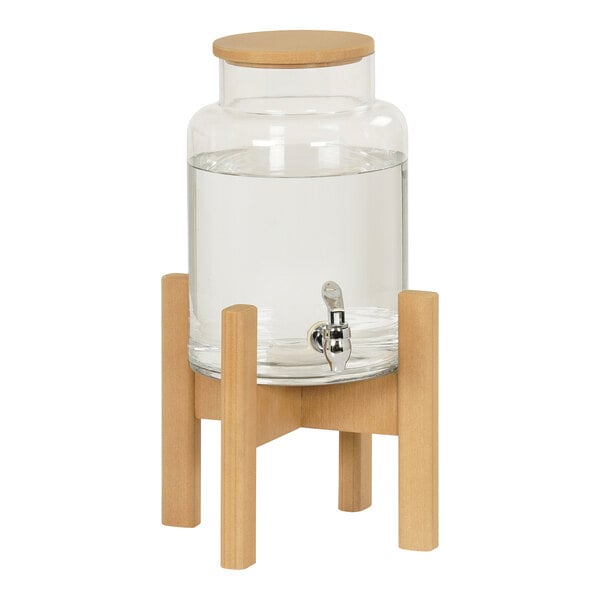 A Cal-Mil round glass beverage dispenser with a faux wood base and a faucet.