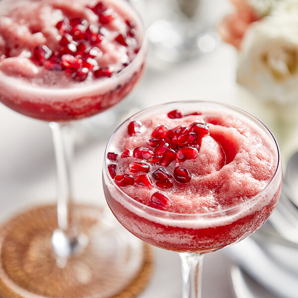 A glass of Perfect Puree Pomegranate concentrate mixed with a pink drink and pomegranate seeds.