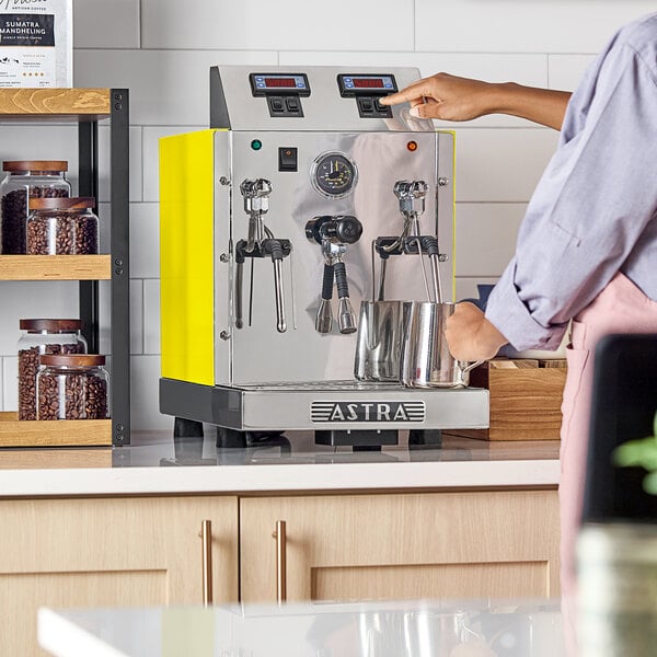 An Astra STA2400-YL gloss yellow automatic milk and beverage steamer with two wands on a countertop.