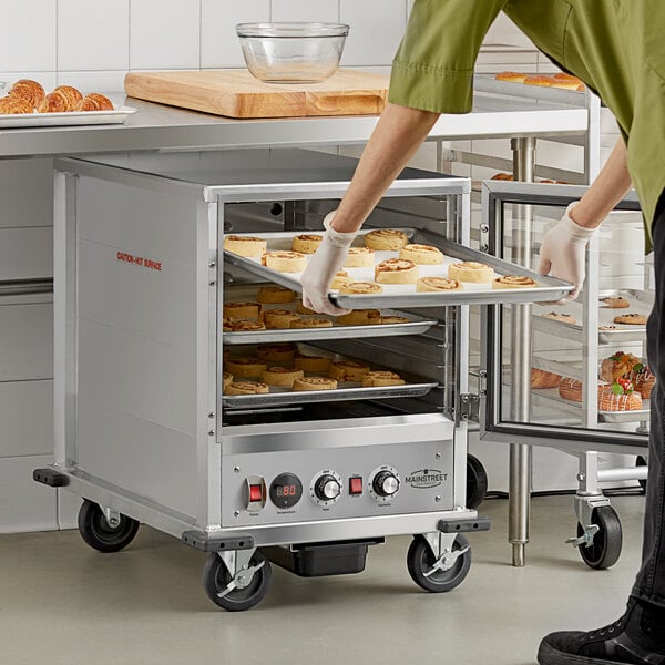 A person holding a tray of food is putting it in a Main Street Equipment heated holding cabinet.