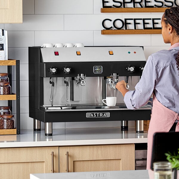 An Astra Mega II M2S-017-GLB semi-automatic black espresso machine on a countertop with a person operating it.