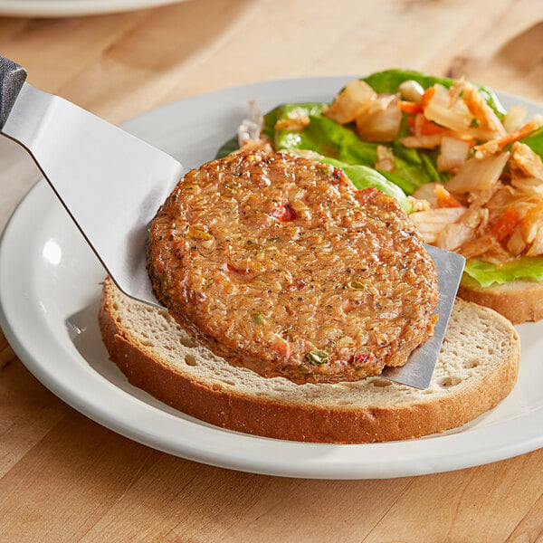 A Gardein veggie burger on a piece of bread with a plate of food and a knife.