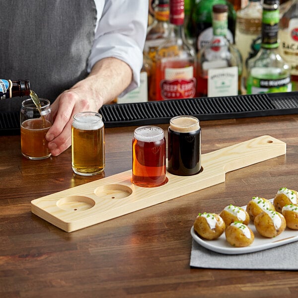 An Acopa natural wood flight paddle holding beer glasses on a table in a bar.