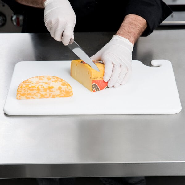A person using a San Jamar color-coded cutting board to cut cheese.