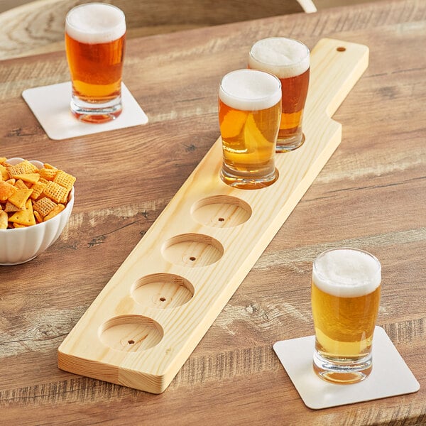 An Acopa natural wood flight paddle holding beer glasses and snacks on a table.