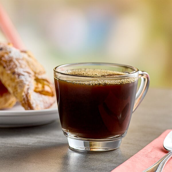 A glass of Folgers Classic Roast coffee with a croissant on a table.