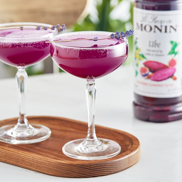 Two glasses of Monin Ube flavored purple liquid on a wooden tray.