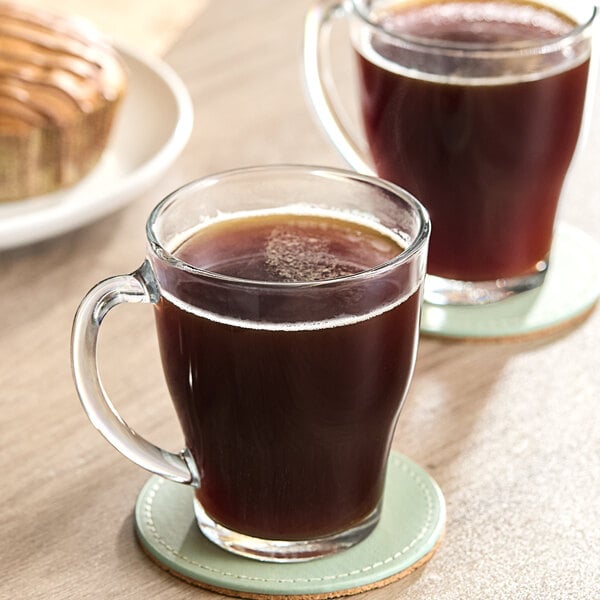 Two glass mugs of brown Pilon espresso on a coaster.