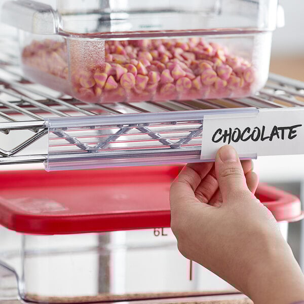 A hand holding a clear label on a shelf.